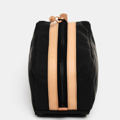 Top view of black toiletry bag with heavy-duty zipper framed by stitched leather strips