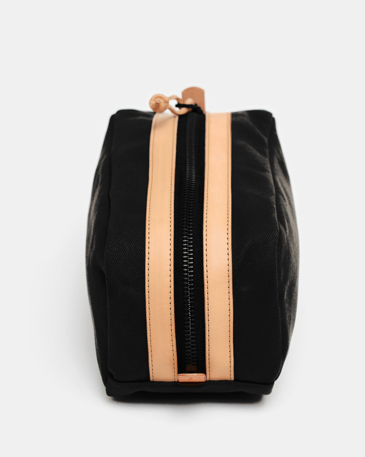 Top view of black toiletry bag with heavy-duty zipper framed by stitched leather strips